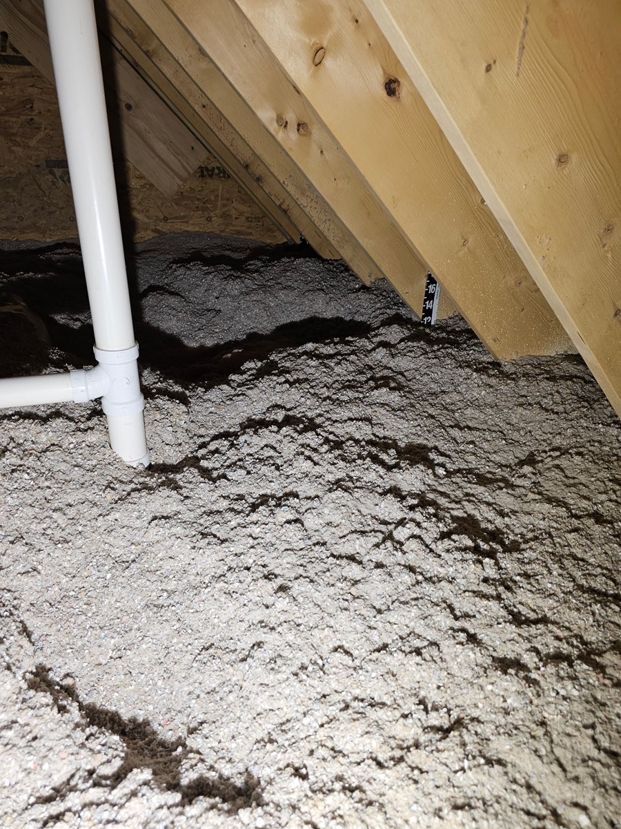 Blown-in cellulose insulation across an attic floor with a depth marker card stapled to a rafter showing the installed inches