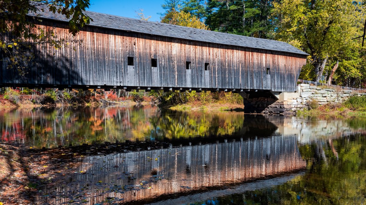 The Hemlock covered bridge reflected in the Saco River in Fryeburg, Maine, in autumn