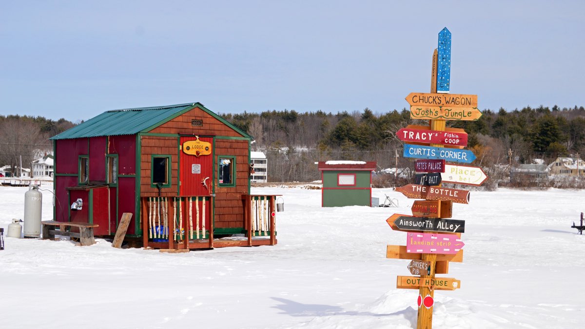 Ice fishing shacks and a hand-painted signpost on the frozen surface of Lake Winnipesaukee, New Hampshire