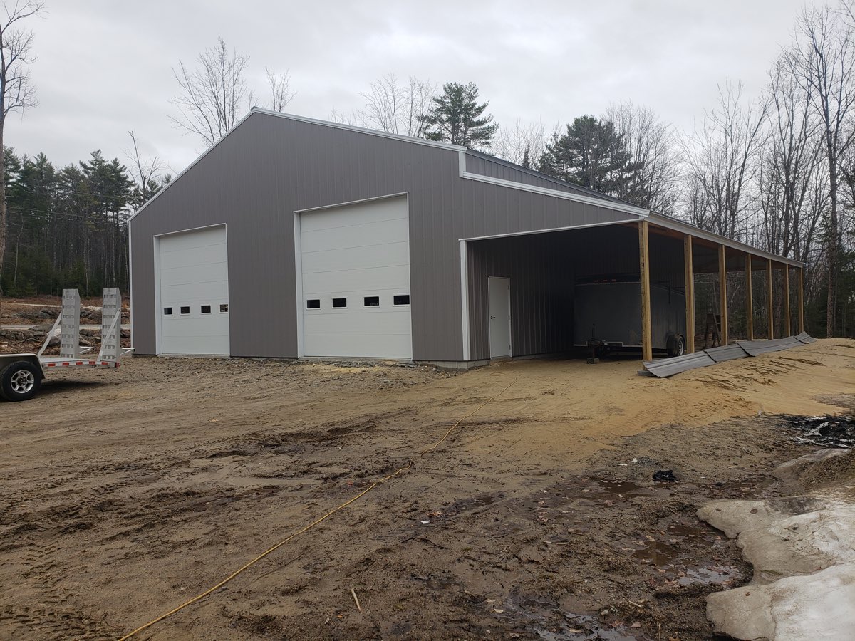 The same pole barn finished, with two overhead doors, grey steel siding and an open equipment bay along one side