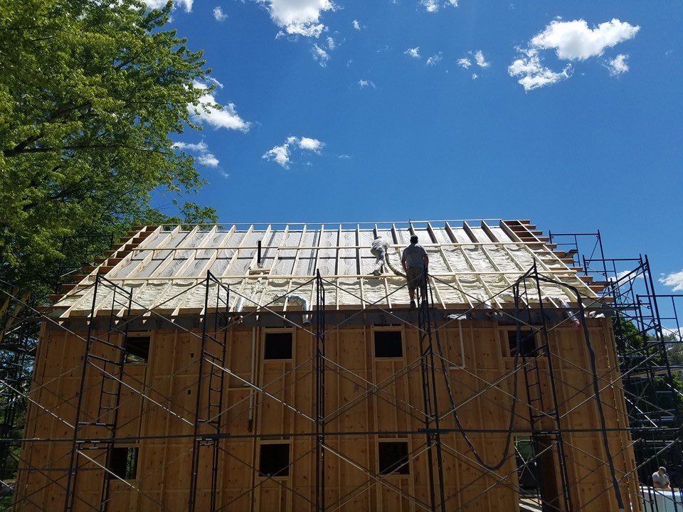 Maine-ly Foam crew spraying foam insulation across an open roof deck on a two-story home in Denmark, Maine