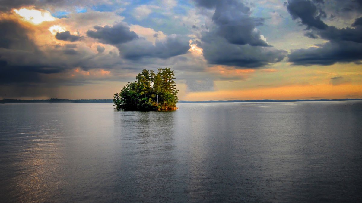 A small wooded island in the middle of Sebago Lake, Maine, at sunset