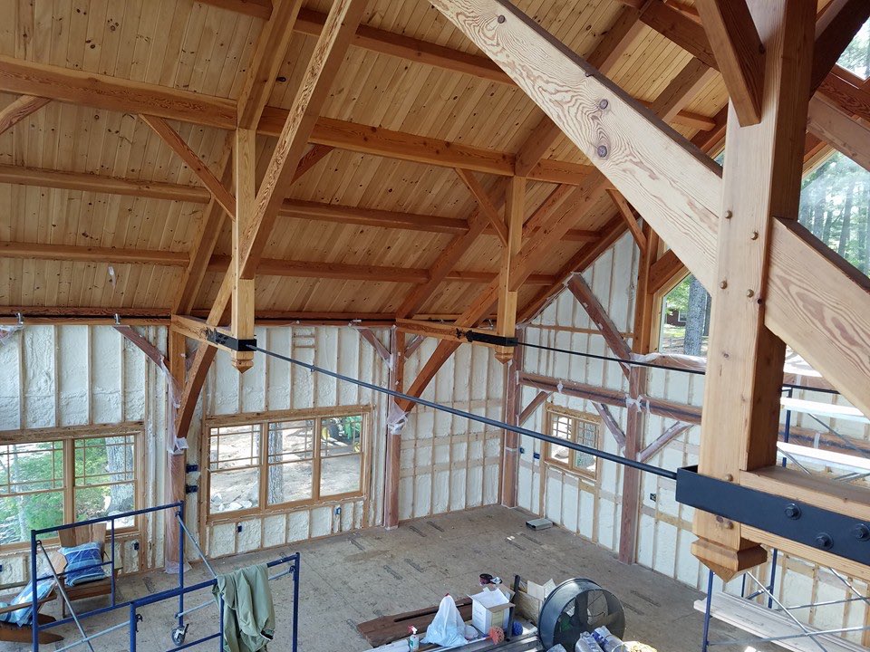 Timber-frame great room with exposed post-and-beam trusses and spray foam insulation applied between the wall studs