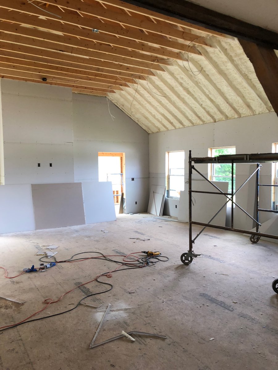 Drywall hung in a vaulted great room, with spray foam insulation still visible on the upper ceiling